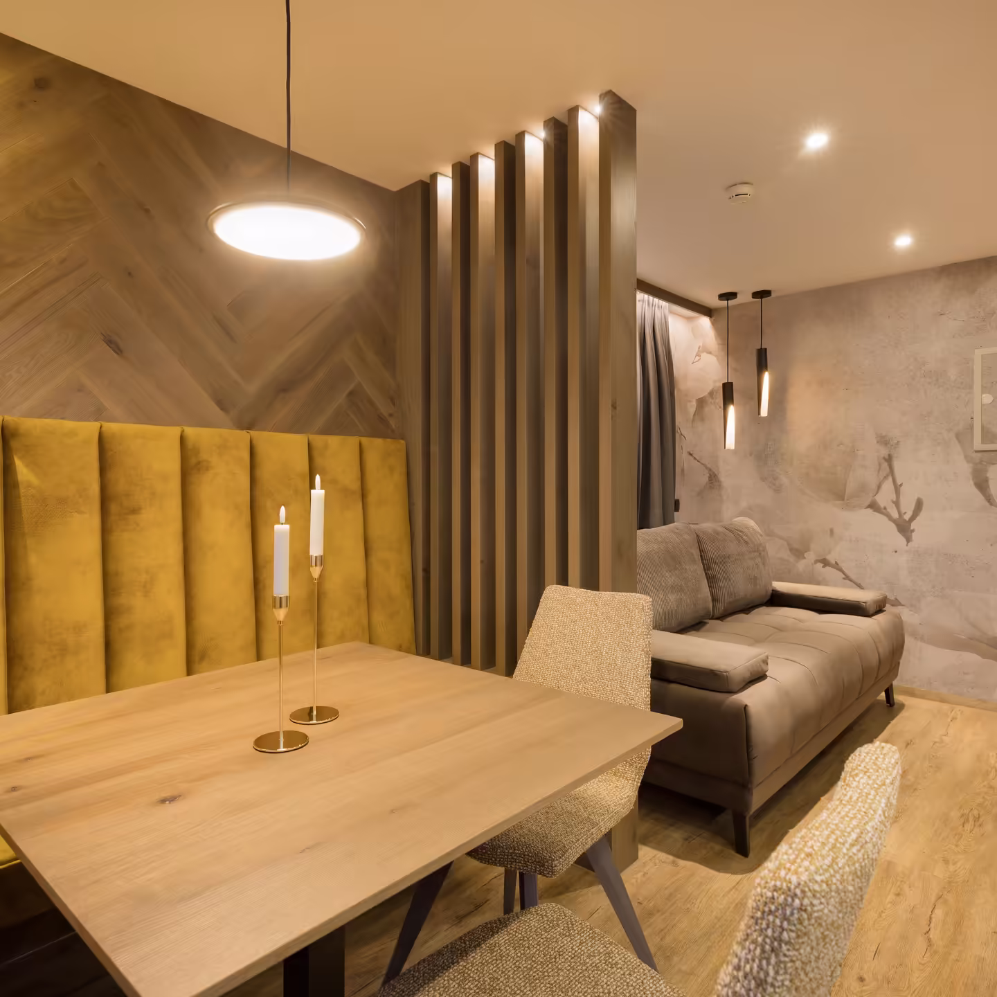 Esstisch mit gelber Sitzbank und großer brauner Couch, getrennt mit Holzpanelen